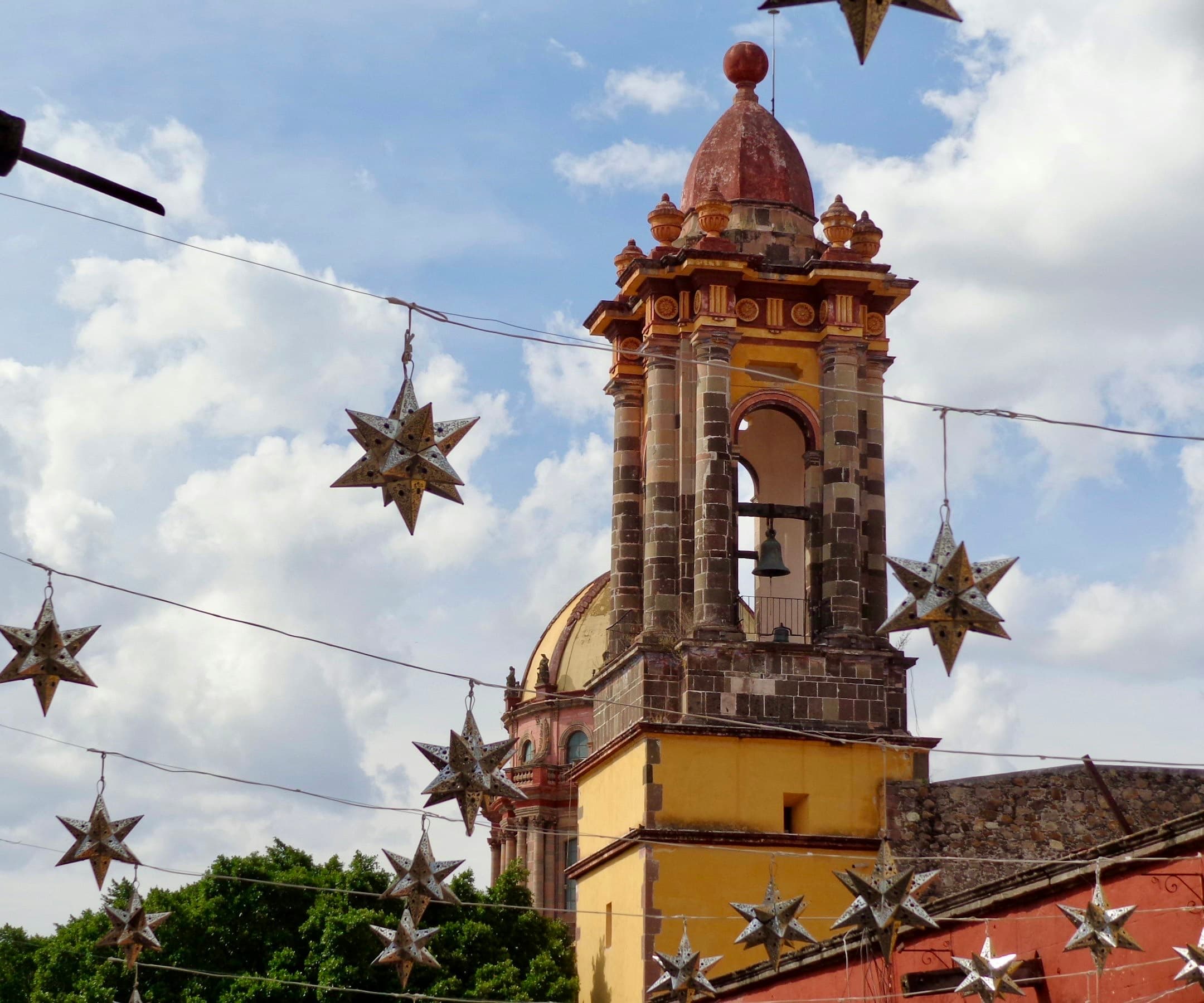 Estrellas de hojalata colgadas sobre una calle, frente al campanario de una iglesia en México